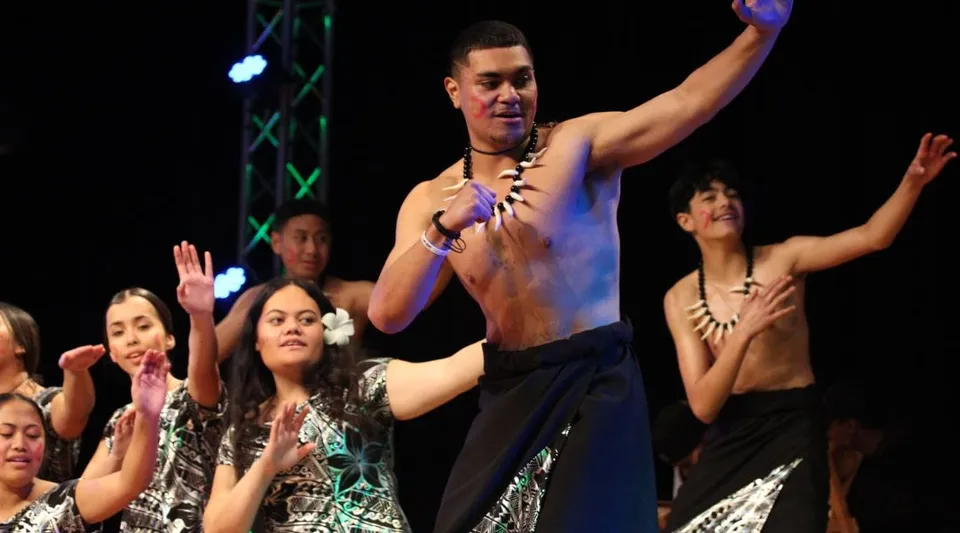 Un performer a torso nudo si trova sul palco davanti a un gruppo di studentesse della Hutt Valley High School con le mani alzate.