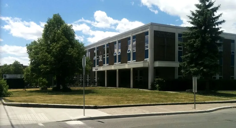 Il moderno edificio a più piani della Notre Dame High School si trova su un terreno erboso con alberi.