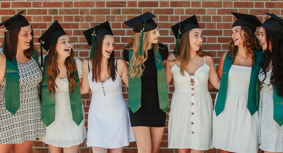 Un gruppo di studentesse in abito da diploma si trova davanti a una parete in mattoni nel campus del Barrie North Collegiate Institute e festeggia il proprio diploma.