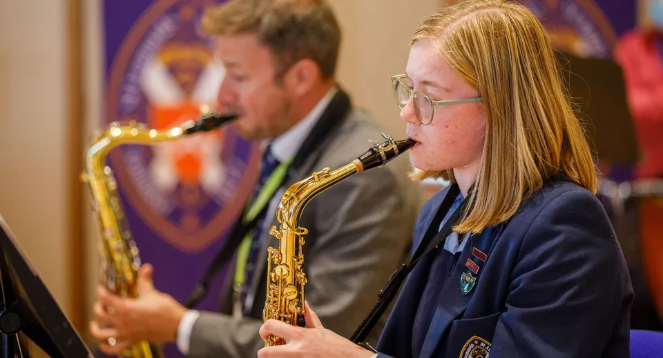 Due studenti della St. Leonards School suonano il sassofono su un palco con uno sfondo viola.