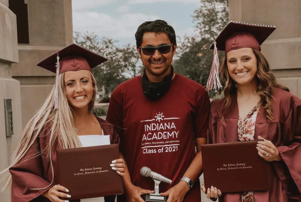 Tre diplomati sorridenti della Indiana Academy for Science, Mathematics and Humanities posano all'aperto con diplomi e un trofeo.