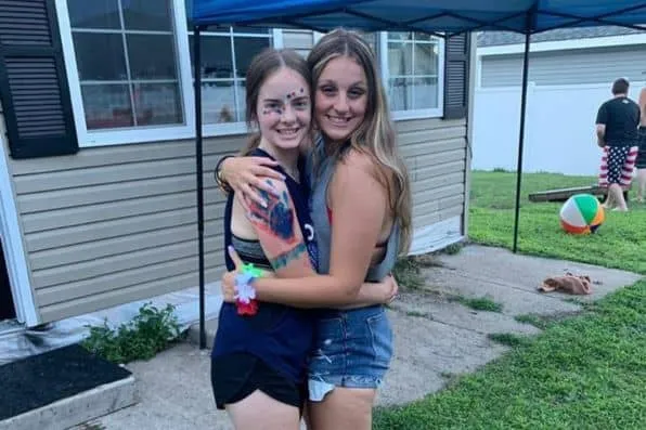 Dos chicas sonrientes con pintura en la piel se abrazan en un jardín