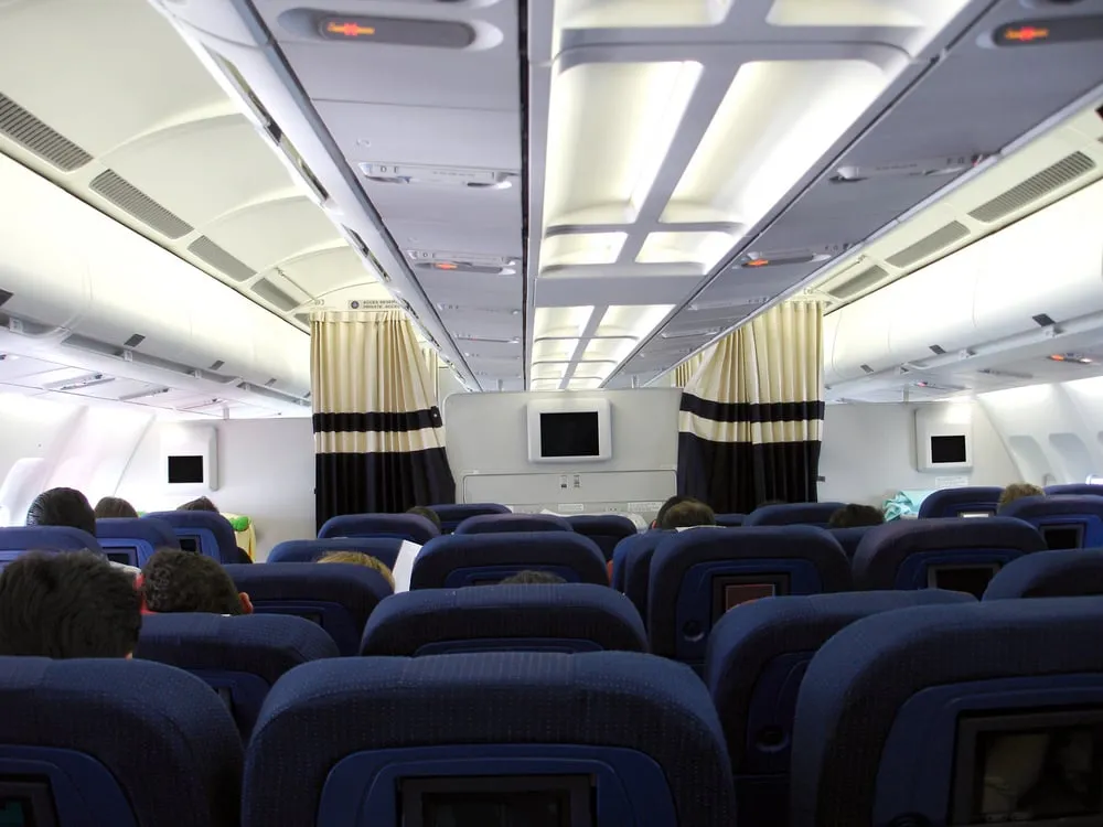 Blick durch den Gang einer Flugzeugkabine mit blauen Sitzreihen und Bildschirmen