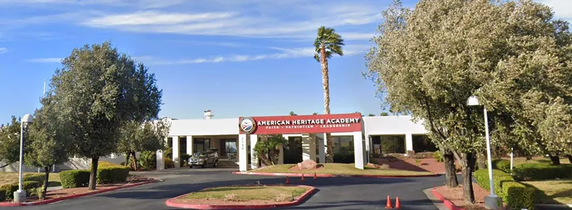 L'edificio della American Heritage Academy con un'insegna rossa e palme in primo piano sotto un cielo azzurro terso.