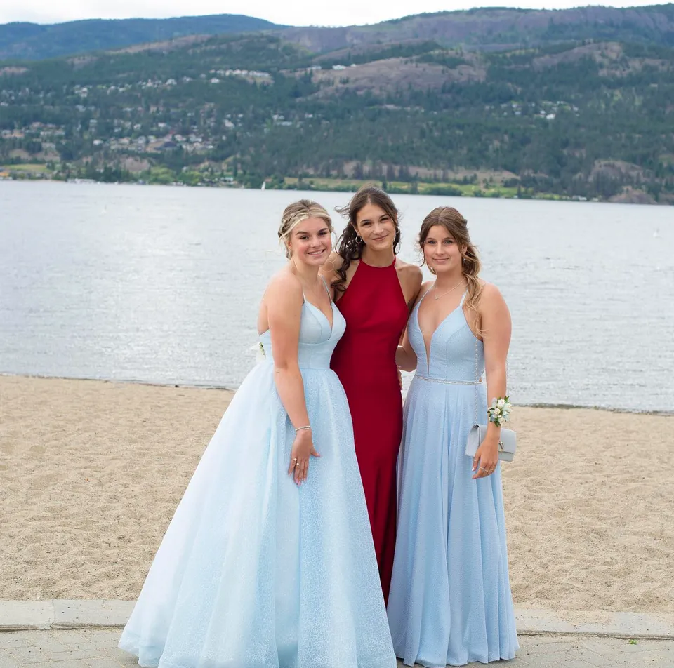 Tre studentesse della Kelowna Secondary School in abito elegante sulla spiaggia con un lago e le montagne sullo sfondo.