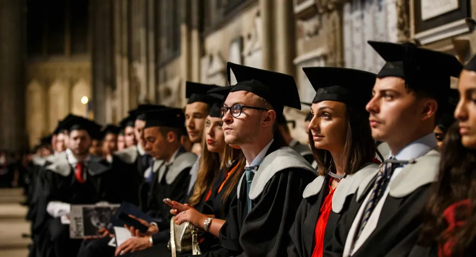 Un gruppo di diplomati in toga e tocco si trova davanti a una struttura decorata nel campus del Kent College.