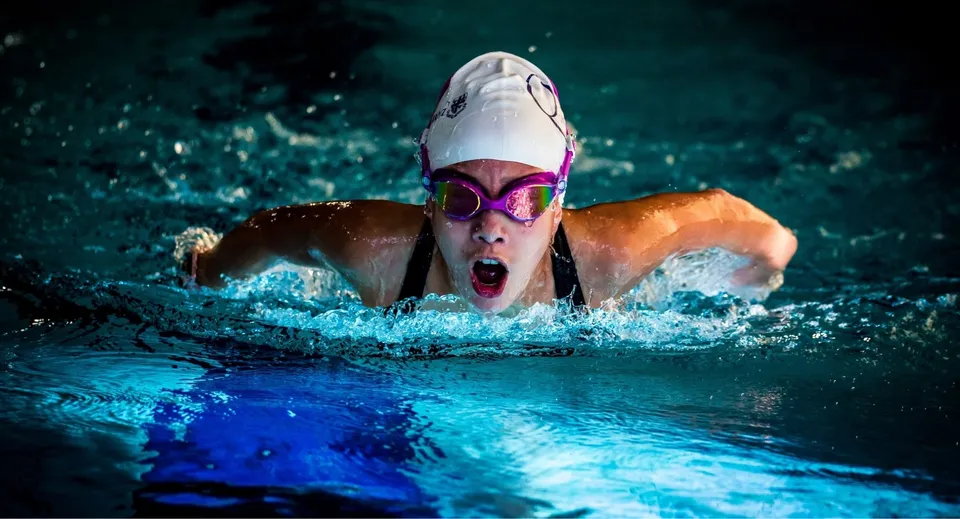 Una nuotatrice con occhialini da nuoto e cuffia rossa mentre nuota con vigore nel campus della Queenswood School.