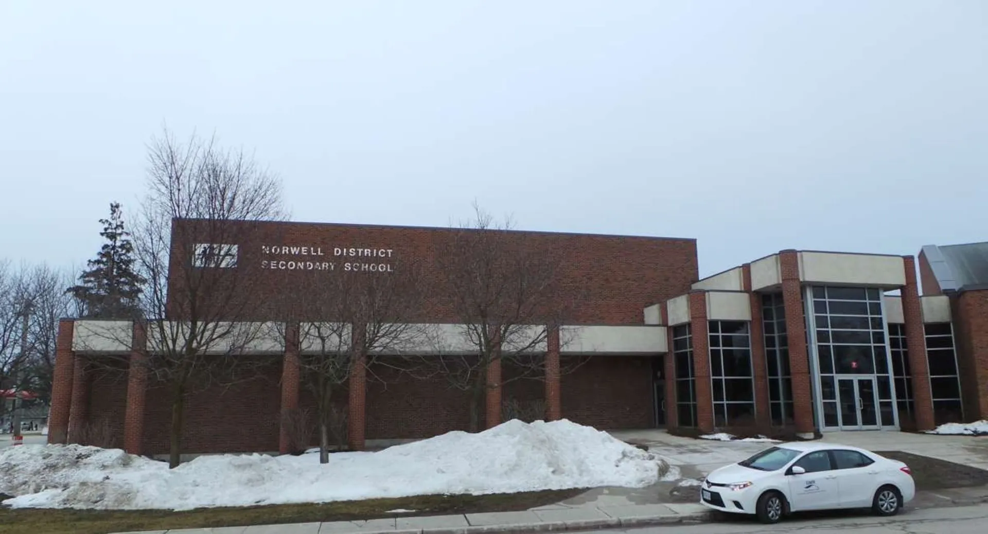 L'edificio in mattoni della Norwell District Secondary School è immerso in un paesaggio innevato con un'auto bianca davanti.