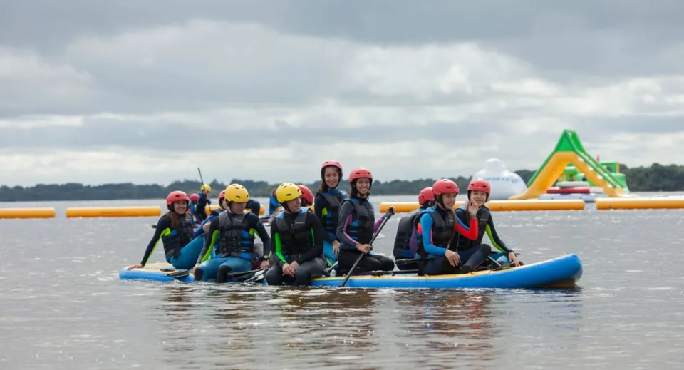 Gli studenti della Castlerea Community School pagaiano insieme su un gommone indossando giubbotti salvagente colorati durante un'attività all'aperto.