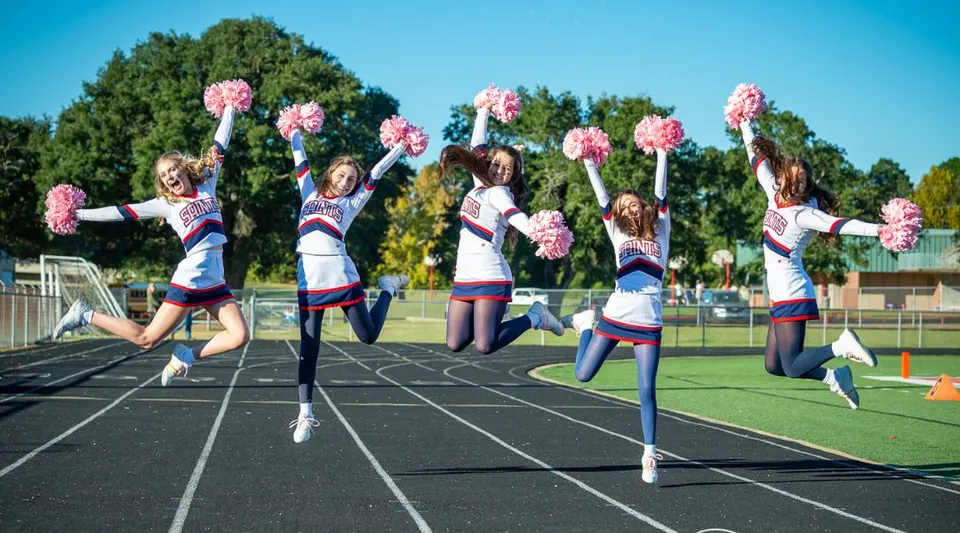 Le studentesse della Academy of the Sacred Heart si esibiscono in una performance di cheerleader sul campo sportivo, immerse nel verde e sotto un cielo blu.