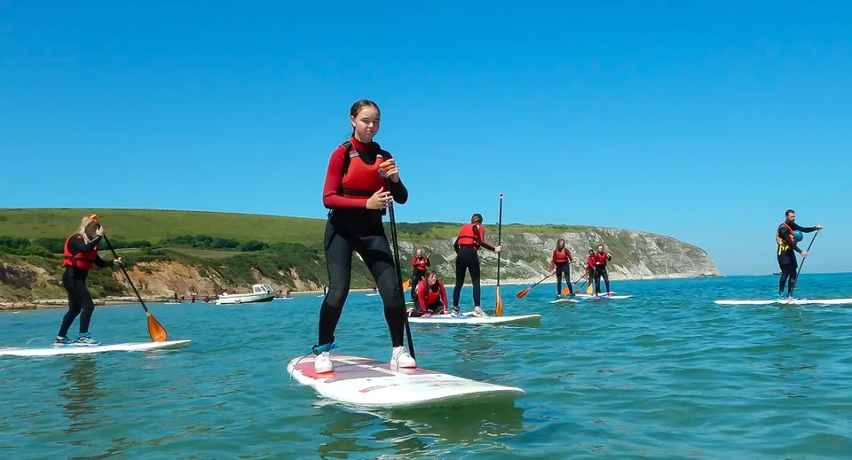 Studenti della Ipswich High School su paddleboard in uno specchio d'acqua con un paesaggio costiero sullo sfondo.