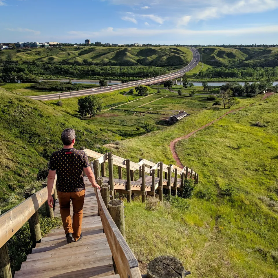 Una persona si trova su una passerella di legno e guarda un paesaggio verde con fiume e strada nel terreno della Chinook High School.