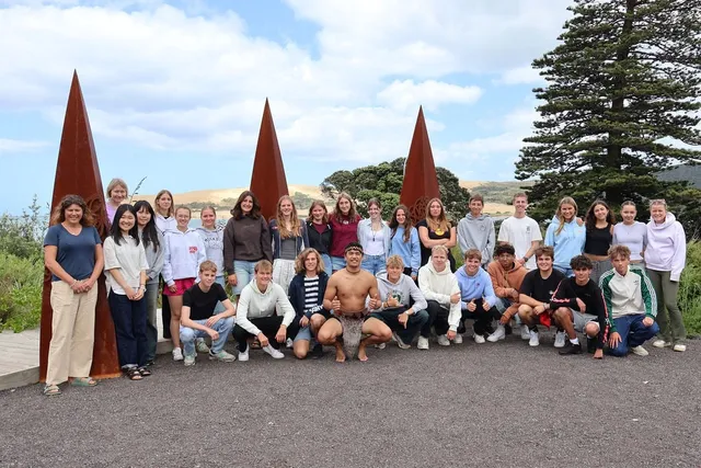 Foto de grupo de estudiantes con un guía maorí ante unas esculturas de madera
