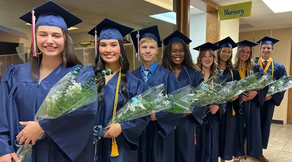 I diplomati della Cadillac Heritage Christian School si trovano nel corridoio con toghe blu e mazzi di fiori.