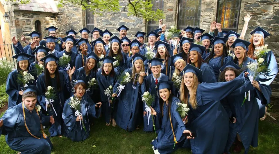 Diplomati e diplomate della Chapel Hill - Chauncy Hall posano all'aperto con la toga blu della cerimonia di diploma davanti a un edificio in pietra.