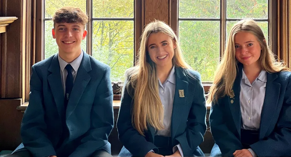 Tre studenti della Lomond School sono in piedi davanti a una grande finestra con vista su alberi e un'area verde.