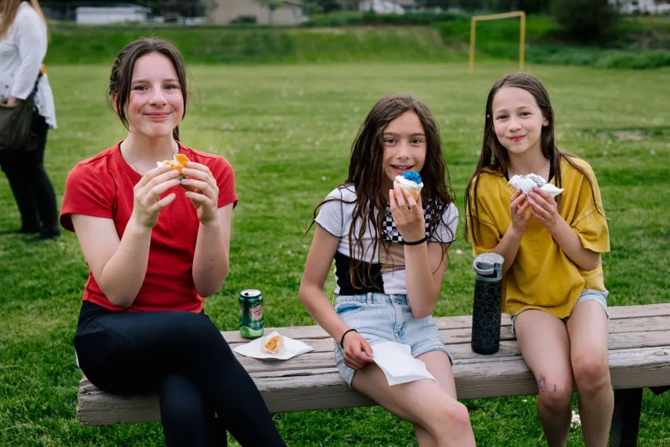 Tre studentesse della École Côte du Soleil siedono su una panchina di legno all'aperto e mangiano un gelato.