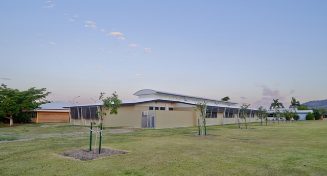 Das moderne Gebäude mit geschwungenem Dach auf dem Gelände der William Ross State High School vor einem grasbewachsenen Feld mit neuen Bäumen.