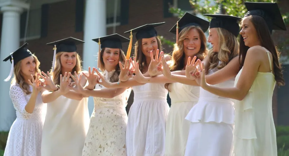 Un gruppo di giovani donne in toghe bianche da laurea festeggia insieme nel campus della St. Margaret’s School.