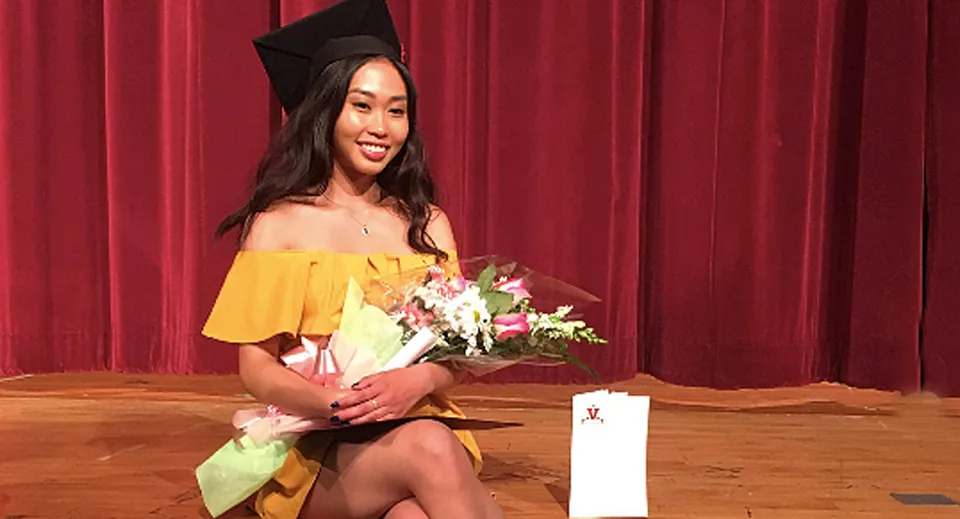 Una diplomata della Georges Vanier Secondary School è in piedi davanti a una tenda rossa e tiene in mano un mazzo di fiori.