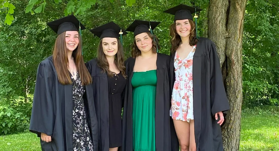 Quattro studentesse in abito da cerimonia di diploma si trovano nel verde nel campus della Elmvale District High School.