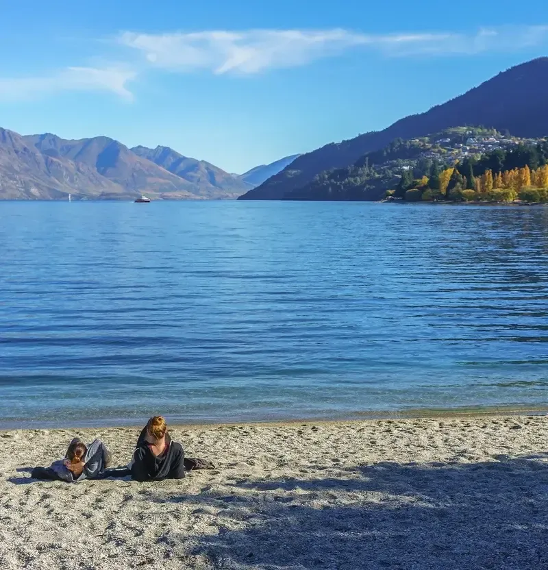 Dos personas descansando en la playa de un lago rodeado de montañas