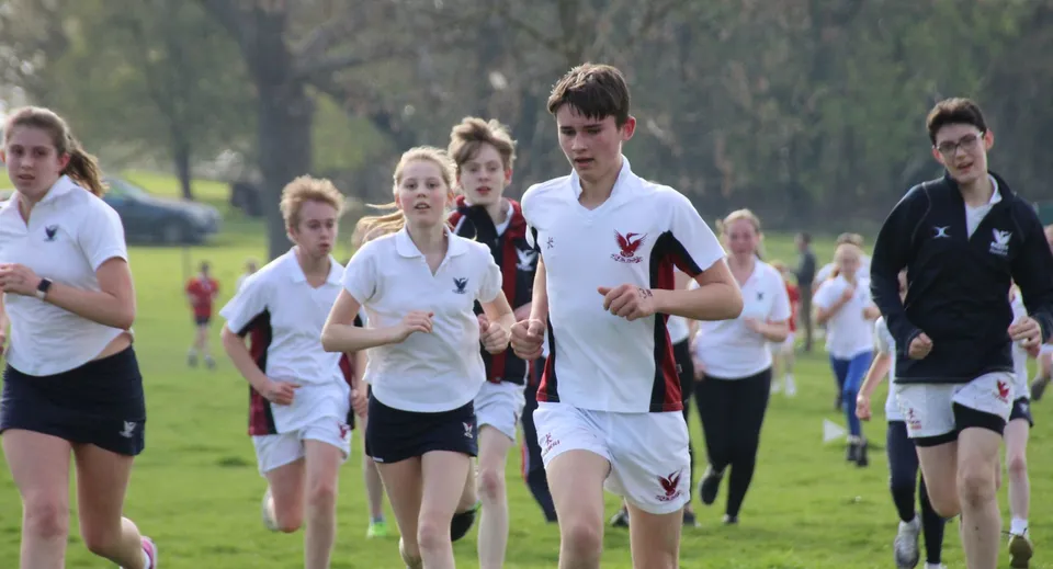 Un gruppo di studenti della Stamford High School corre insieme sul campo sportivo tra gli alberi.