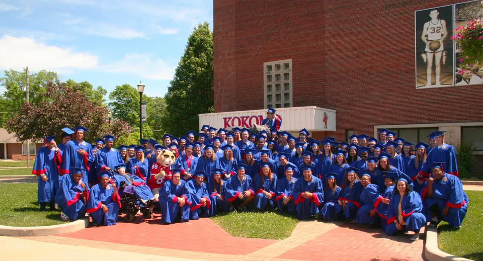 Diplomati e diplomate della Kokomo High School in toga blu davanti a un edificio in mattoni all'aperto.