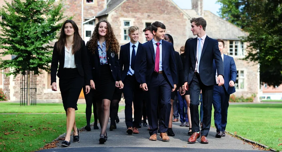 Un gruppo di studenti del King’s College cammina insieme su un viale circondato dal verde e da un edificio storico.