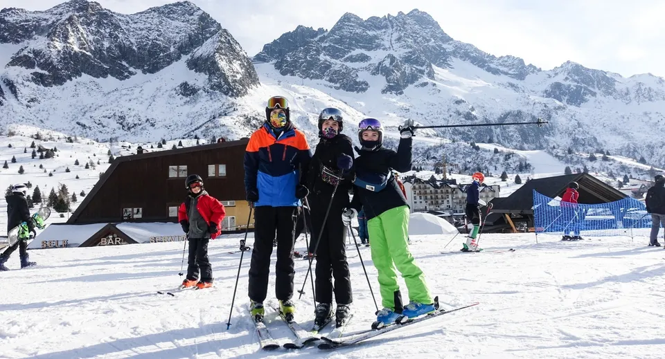 Un gruppo di studenti del St. David's Catholic Sixth Form College in posa davanti a un paesaggio montano innevato con uno chalet sullo sfondo.