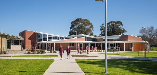 Das moderne Gebäude der Underdale High School ist von einer Wiese und Bäumen umgeben, vor dem Haupteingang laufen mehrere Personen auf einem Weg.