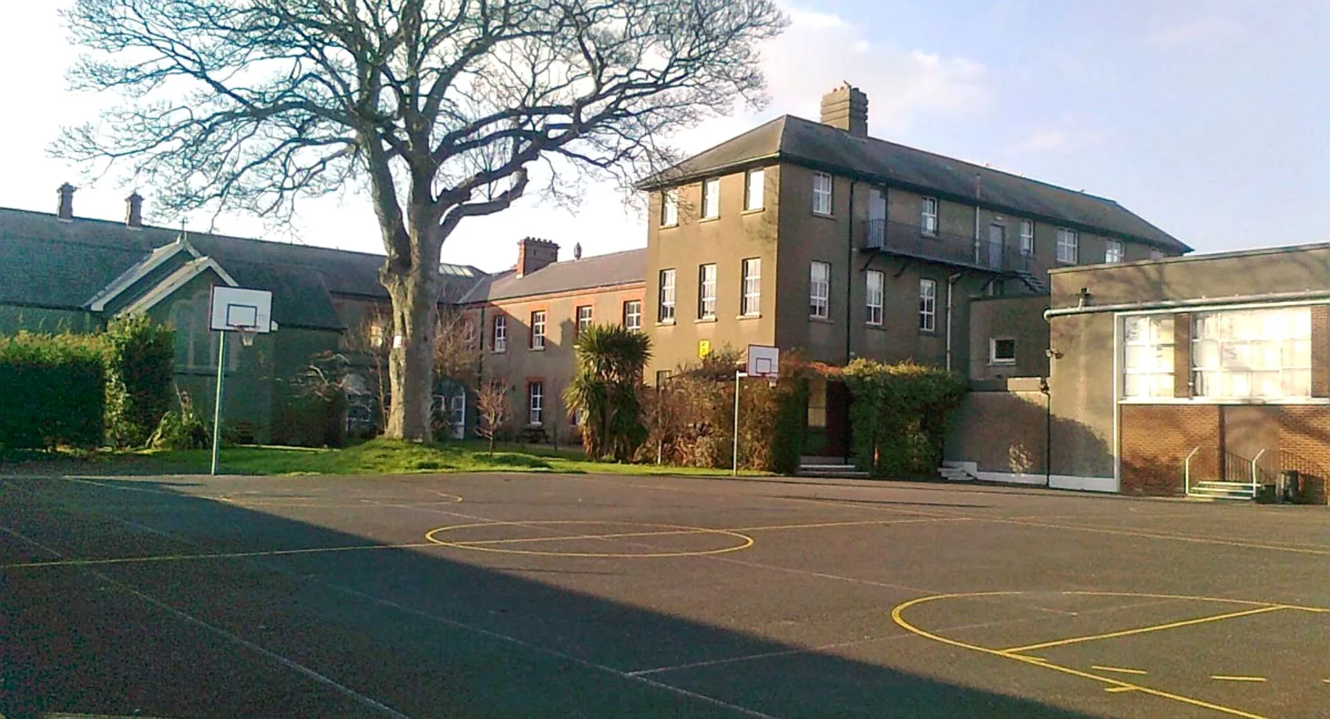 L'edificio in mattoni a più piani della St. Mary’s Secondary School a Baldoyle con un campo da basket in primo piano e circondato da alberi.
