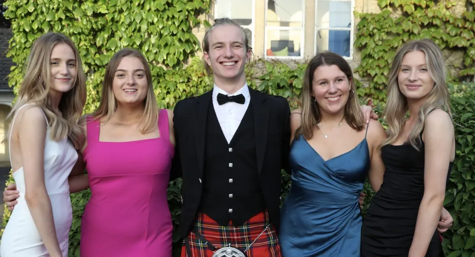 Un gruppo di cinque persone vestite in modo formale si trova davanti a una parete ricoperta di verde nel campus della Warminster School.