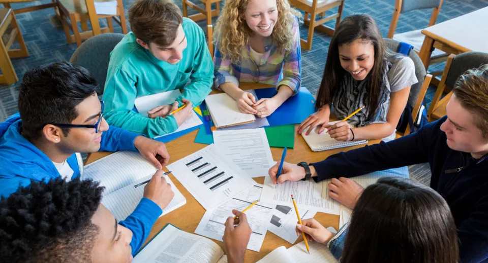 Studenti della Blackwater Community School lavorano insieme a un tavolo con libri di testo e schede didattiche.