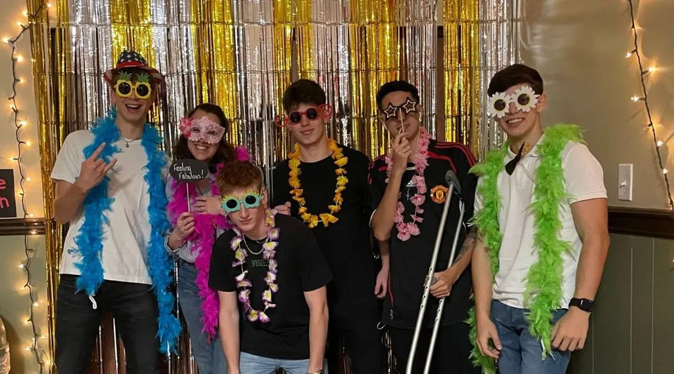 Un gruppo di studenti della The Phelps School posa davanti a uno sfondo di tende dorate e argentate in abiti festivi colorati.