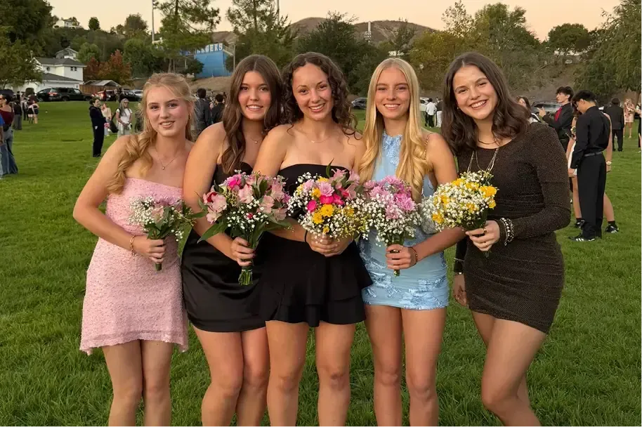 Cinco chicas con vestido de gala y ramos de flores en una fiesta escolar al atardecer