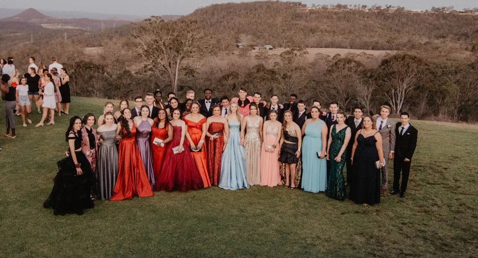 Un grande gruppo di studenti del Highlands Christian College si trova su un prato davanti a un paesaggio montuoso.