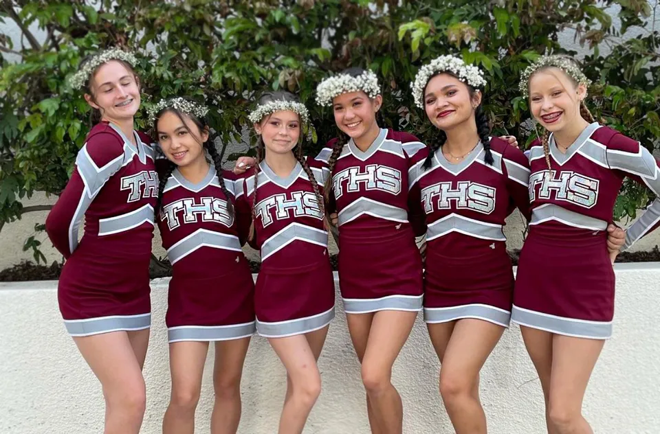Un gruppo di studentesse della Torrance High School in uniformi da cheerleader con corone di fiori posa all'aperto su uno sfondo verde.