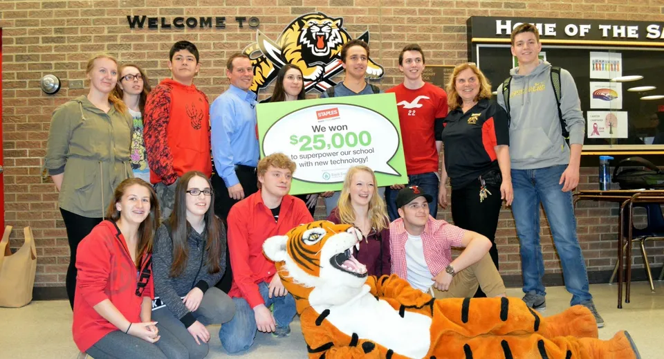 Studenti e adulti della Saunders Secondary School consegnano un grande assegno da 25.000 dollari US durante una cerimonia.
