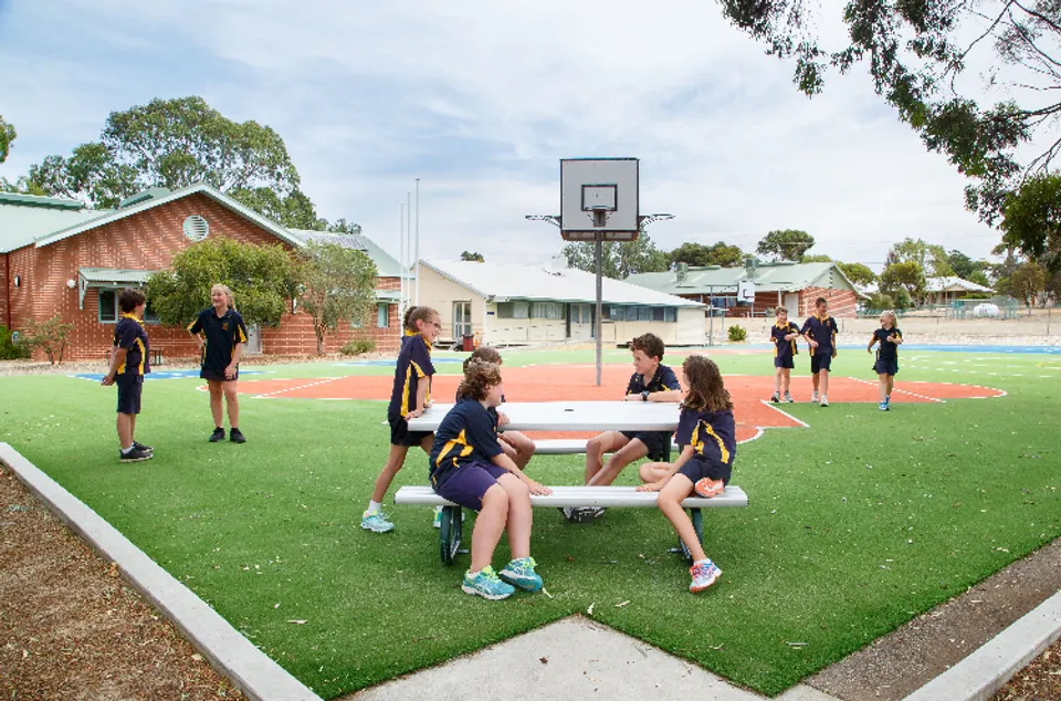 Un gruppo di studenti gioca a basket sul campo sportivo della Ravensthorpe District High School, circondato da edifici in mattoni e alberi.