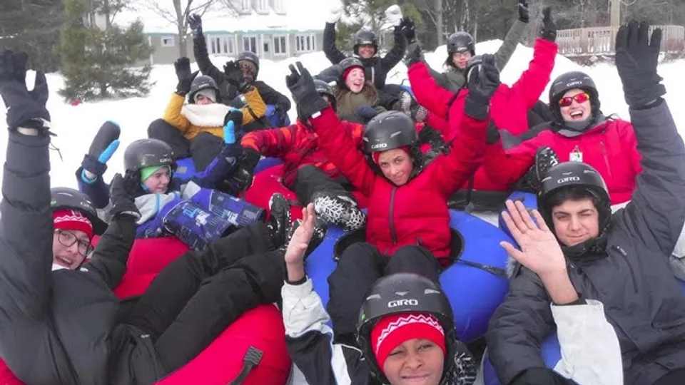 Un gruppo di studenti della École secondaire publique Omer-Deslauriers si trova all'aperto nella neve davanti agli edifici, indossando abiti invernali colorati.