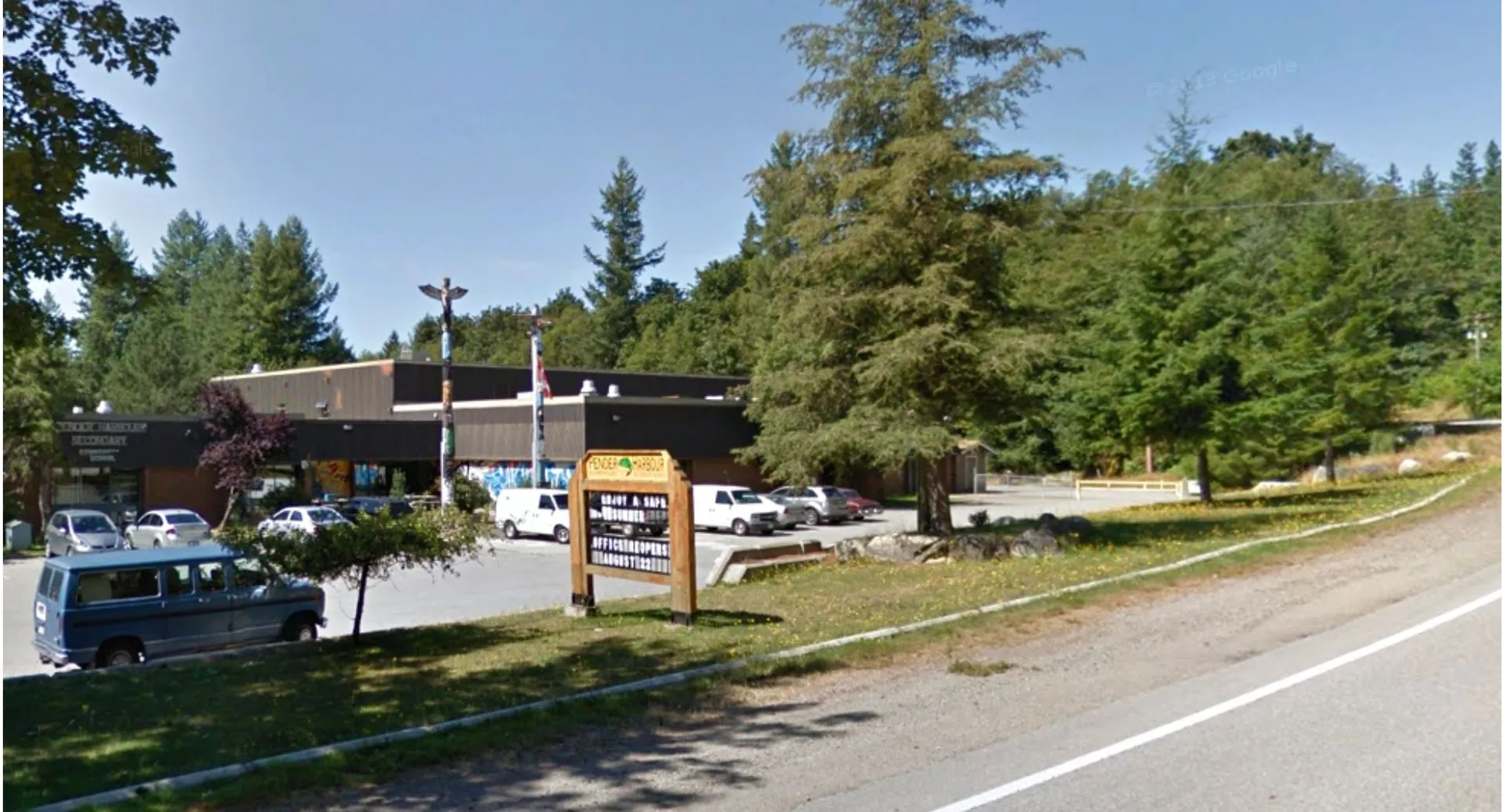 L'edificio scolastico della Pender Harbour Secondary con parcheggio, totem e alberi sullo sfondo.