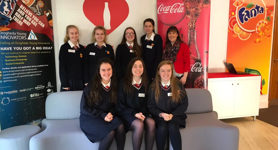 Un gruppo di studentesse della Sacred Heart Secondary School a Drogheda posa davanti a sfondi pubblicitari di Coca-Cola e Fanta.