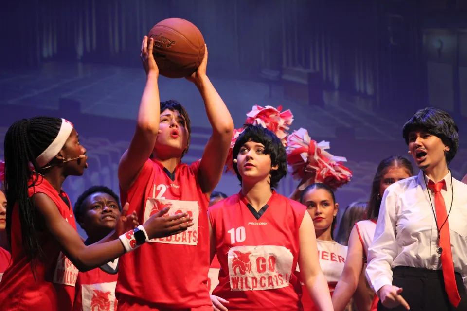 Un gruppo di studentesse e studenti della St. Joseph’s Secondary School a Castlebar si trova su un palco con maglie rosse e un pallone da basket davanti a uno sfondo colorato.