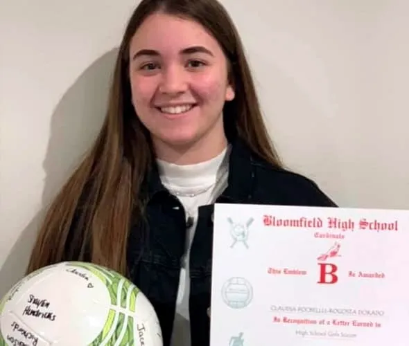 Chica joven sonriente sosteniendo un balón firmado y un certificado escolar de Bloomfield High School