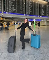 Junge Frau posiert mit zwei Koffern vor den Anzeigetafeln einer Flughafenhalle