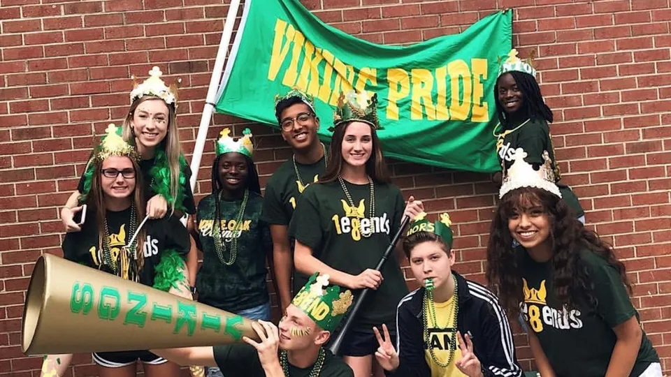 Un gruppo di studenti della White Oaks Secondary School si trova davanti a un muro di mattoni tenendo una bandiera verde con la scritta MAINE PRIDE.