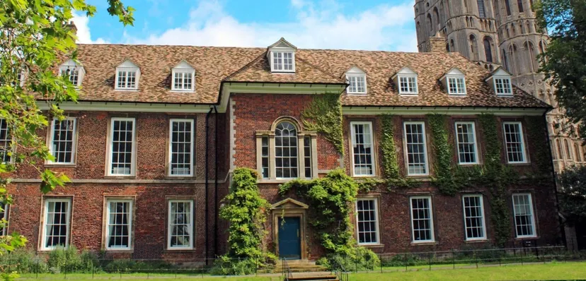 L'edificio in mattoni di King's Ely è circondato da piante verdi e si staglia sotto un cielo azzurro e limpido.