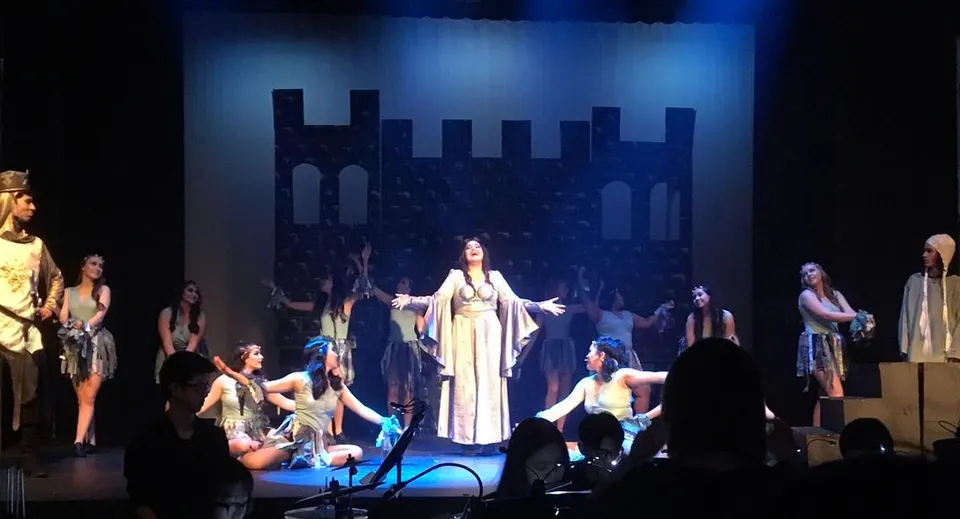 Gli studenti della Pinetree Secondary School recitano uno spettacolo teatrale in costume su un palco illuminato.