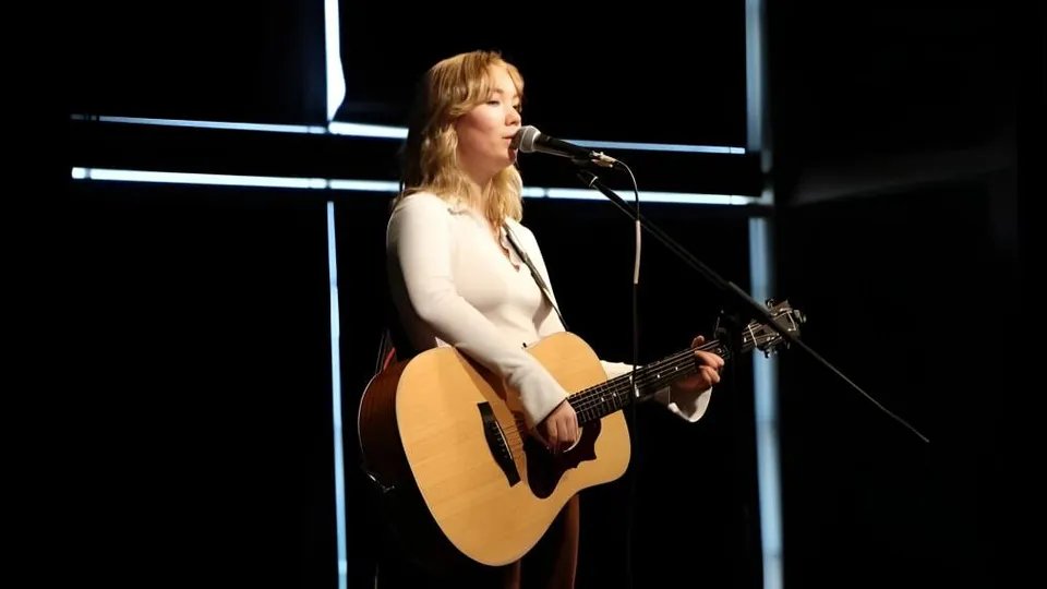 Una studentessa della École L’Odyssée suona la chitarra e canta durante un'esibizione sul palco.